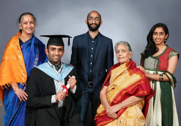 Vishal sitting with 4 of his family members, dressed up for his graduation and holding his degree scroll.