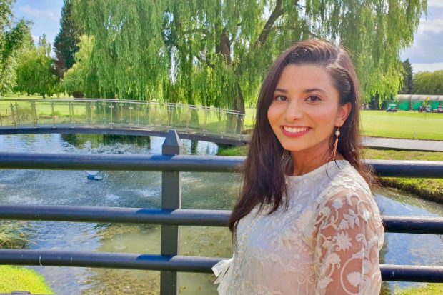 Tasqeen standing on a bridge with a lake and tress behind her. 