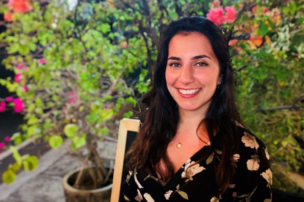 Farah, smiling at the camera and standing in front of some plants.