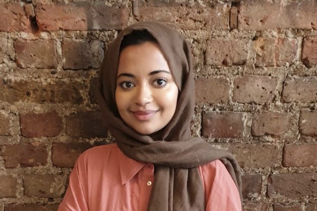 Samiha standing in front of a brick wall, smiling at the camera. 