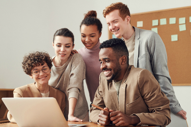 People standing around and look at a laptop.