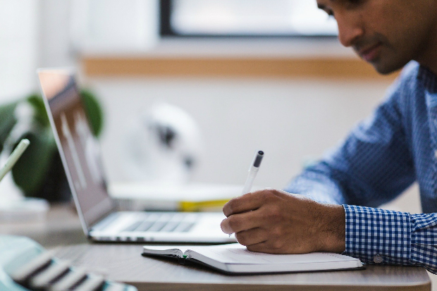 A man sitting at his desk and writing in a note pad.