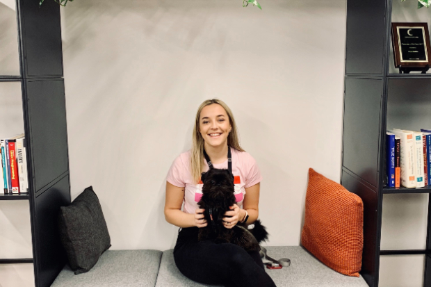 Elle sitting on a seat, smiling at the camera and holding a small dog on her lap.