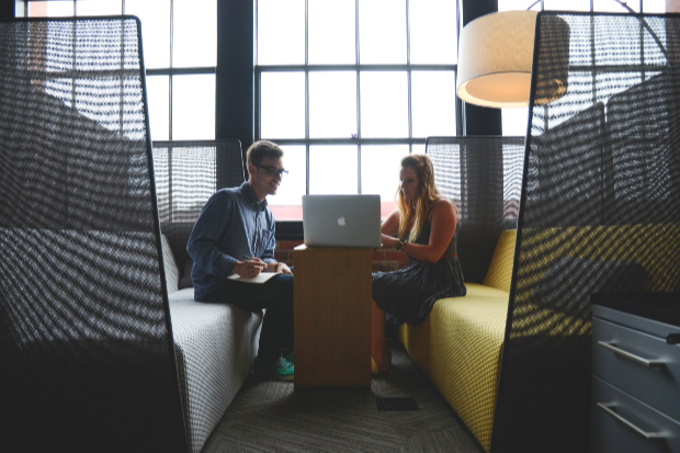 Two people sitting at a desk and looking at a laptop.